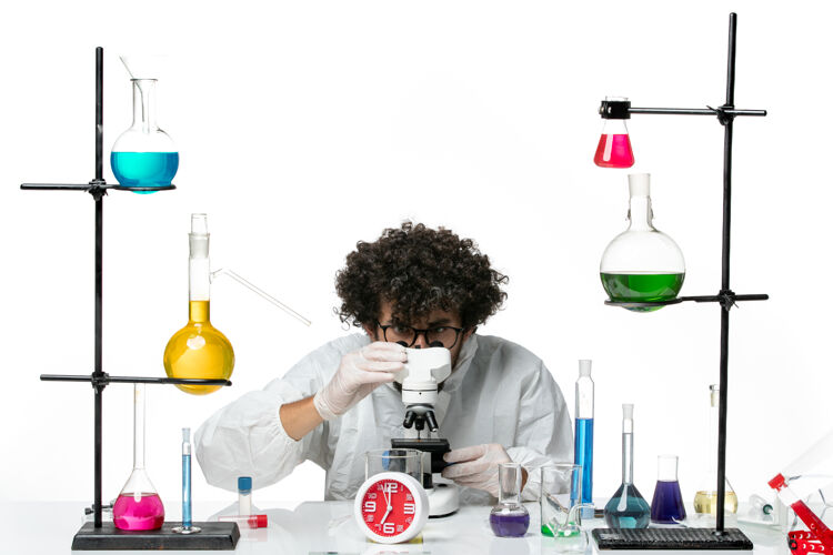 视图正面图穿着白色特别套装的年轻男科学家正在尝试使用显微镜显微镜瓶子容器