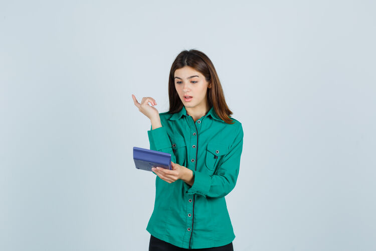 积极年轻的女士一边看着计算器 一边展示着身着绿色衬衫的尤里卡手势 一边惊讶地看着前视图漂亮成人时尚