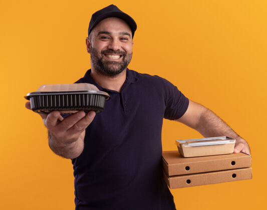 送货微笑的中年送货员身着制服 戴着帽子 手里拿着披萨盒 手里拿着隔离在黄色墙上的食品容器微笑中年人披萨