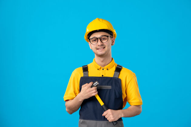 工作身穿制服的男建筑工人手拿锤子在蓝色墙上的正视图建筑商服务蓝色