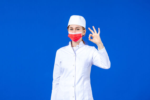 正面正面图身着医疗服的年轻护士 蓝色墙上戴着红色防护面具医疗防护红色