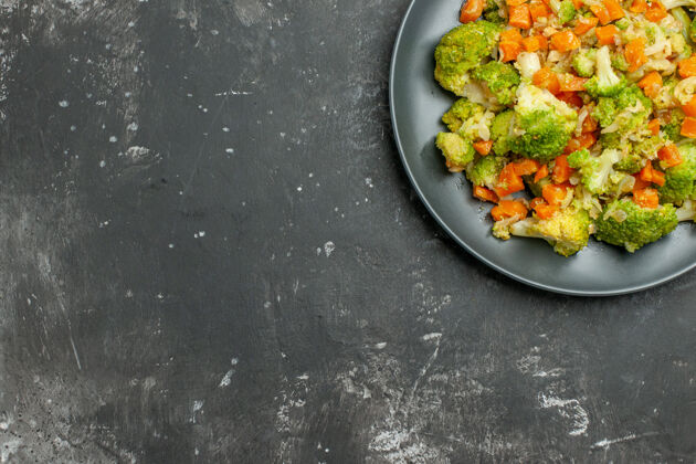 美食在灰色桌子上的黑色盘子上放半杯健康的西兰花和胡萝卜午餐蔬菜晚餐