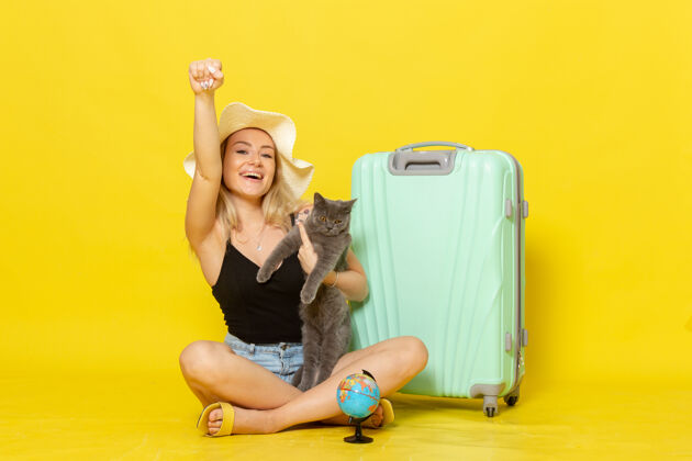 颜色正面图年轻的女性坐在她的绿色袋子抱着小猫在淡黄色的墙上旅行度假旅行海色旅行太阳海光猫