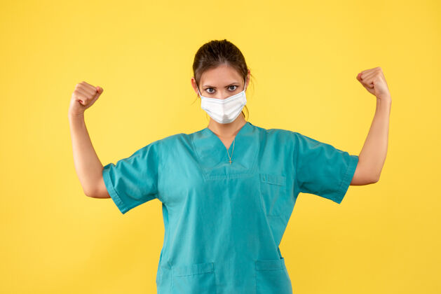 肖像正面图黄色背景上穿着医用衬衫和无菌口罩的女医生人病毒女医生