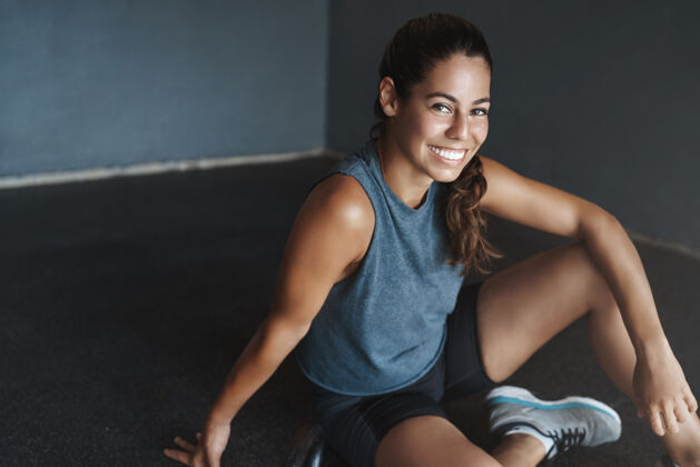年轻坐在健身房地板上的巴西年轻漂亮女人运动装运动员满意