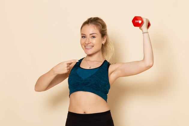 运动正面图身穿运动装的年轻女性手持哑铃在白墙上运动身体健康美容锻炼的女人服装视野健身