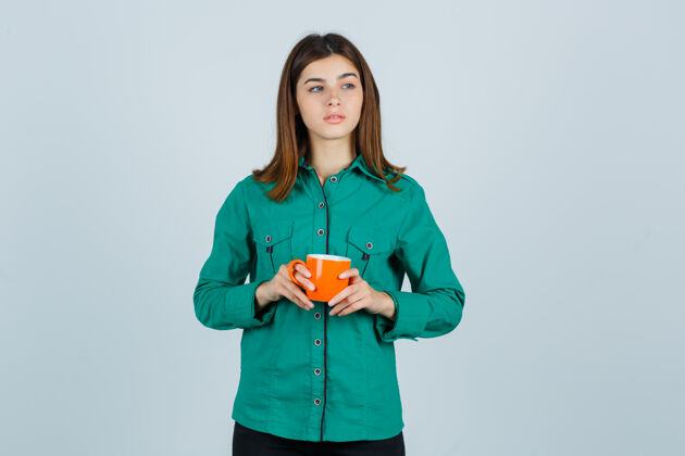 护理年轻的女士拿着一杯橘色的茶 穿着衬衫 看起来很专注衬衫皮肤茶