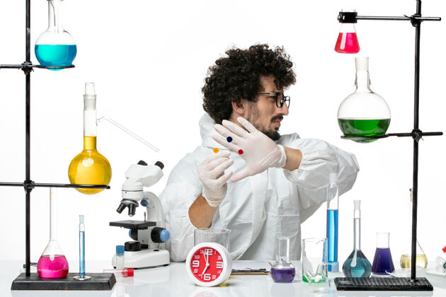套装正面图身着特殊套装的年轻男性科学家围着桌子工作 白墙上有解决方案科学医生实验室