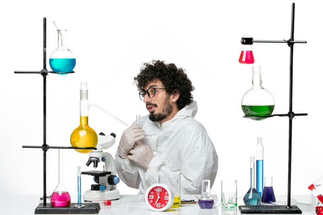 烧瓶正面图：年轻的男科学家穿着特制的衣服 拿着装有溶液的烧瓶 挂在浅白的墙上烧杯光化学