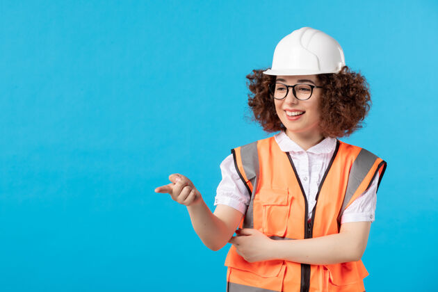 人穿着制服的女建筑工人正对着蓝色墙上的东西指尖女建筑工人蓝