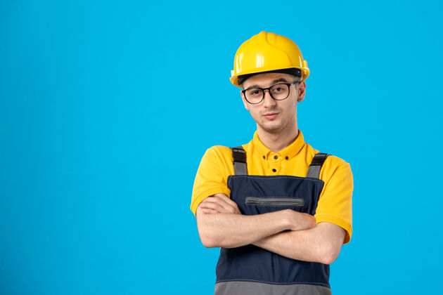 前面蓝色墙壁上穿着制服和头盔的男建筑工人的正视图建筑工承包商杂工