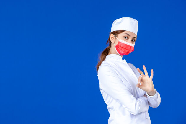 病毒正面图蓝色墙上戴着红色面罩的年轻护士 穿着医疗服面罩红色Ok标志