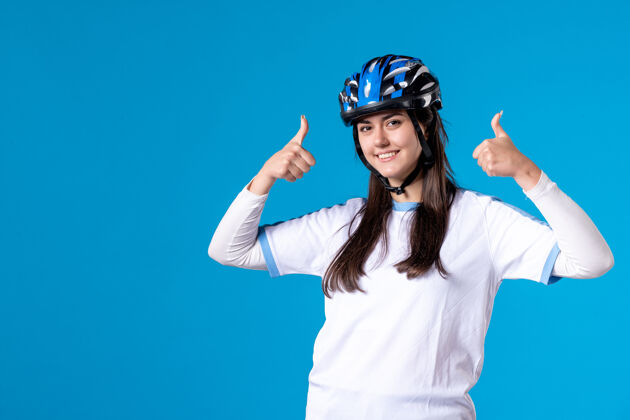 竖起大拇指前视图穿着运动服的年轻女性 蓝色墙上戴着头盔视图人物人物