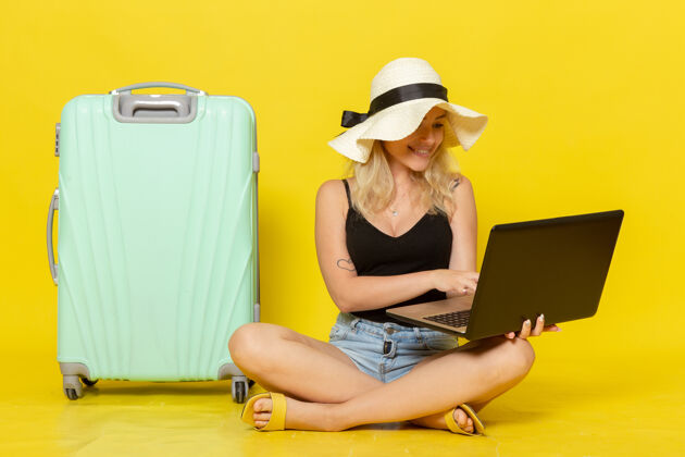 休闲正面图年轻女性在黄墙上使用笔记本电脑女孩远航度假旅行旅行太阳成人年轻视野