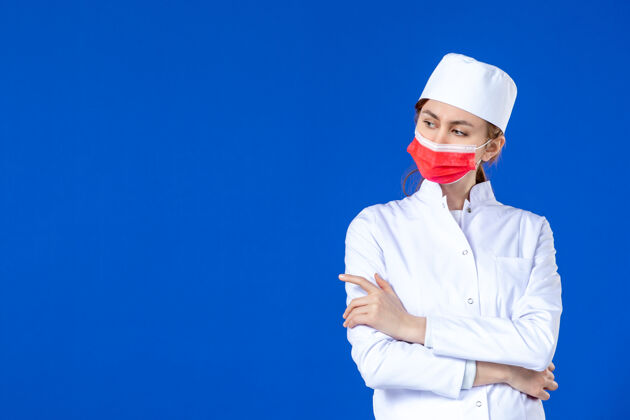 蓝色正面图蓝色墙上戴着红色面罩的年轻护士 穿着医疗服医学医院正面