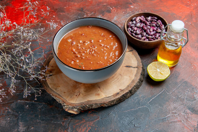 木头番茄汤放在蓝色的碗里放在棕色的木托盘上豆子油瓶放在五颜六色的桌子上托盘果汁西红柿汤