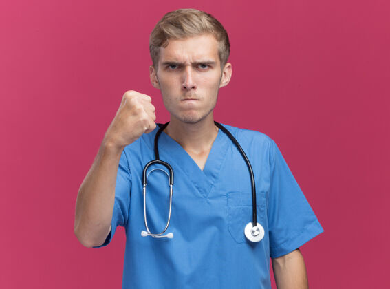 制服严格的年轻男性医生穿着医生制服 手持听诊器 拳头隔离在粉色墙壁上 留有复印空间佩戴听诊器手持