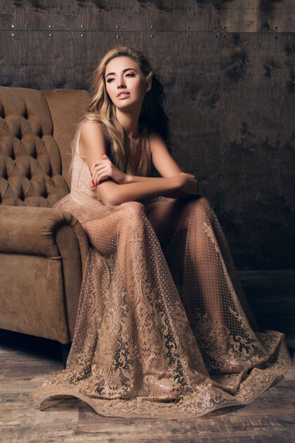 衣服穿着闪亮蕾丝晚礼服的美丽性感模特坐在米色的椅子上姿势诱惑华丽