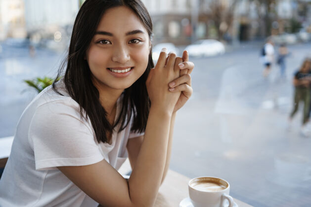 杯子美丽的自然女子独自在咖啡馆里喝咖啡 坐在窗边 对着镜头开心地微笑人年轻人女孩