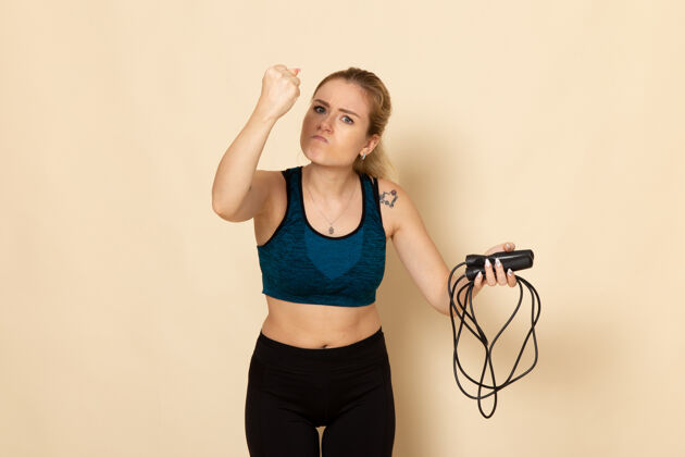 年轻女性正面图身穿运动装的年轻女性手持跳绳 在白墙上生气健身操身体运动美容操运动感觉跳跃