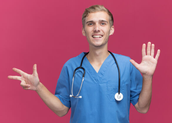 男性微笑的年轻男医生穿着医生制服 听诊器显示不同的数字隔离在粉红色的墙上展示年轻制服