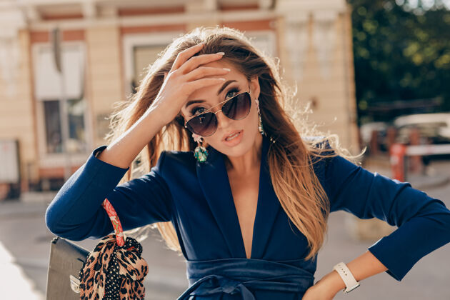 时尚优雅迷人的女人穿着蓝色时尚西装 戴着墨镜 手拿手袋走在街上阳光套装眼镜