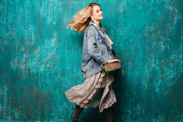 女性性感迷人的金发女郎穿着牛仔裤和超大夹克在街上与复古绿色的华尔街对峙外套五月季节