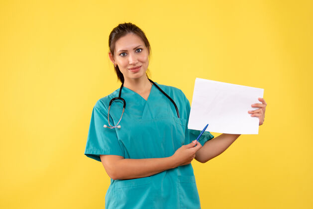 正面正面图黄色背景下穿着医疗衫的女医生拿着纸分析健康听诊器黄色