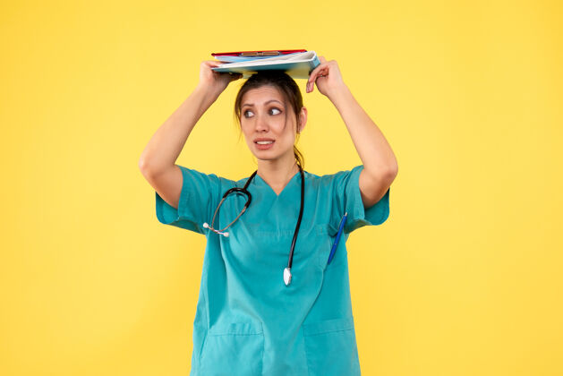 医生前视图穿着医用衬衫的女医生拿着黄色背景的笔记持有专业药