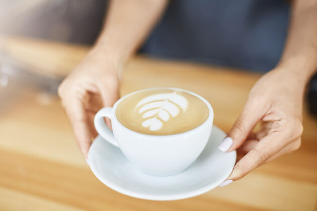 加油站特写镜头的妇女手服务卡布奇诺在一个杯子与拿铁艺术咖啡师的概念学生咖啡员工