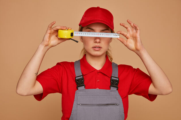 胶带严肃的年轻女建筑工人戴着帽子 穿着制服 眼前拿着卷尺眼睛制服严重