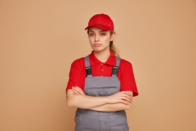 女严肃的年轻女建筑工人 穿着制服 戴着帽子 站着 保持封闭的姿势站着帽子姿势