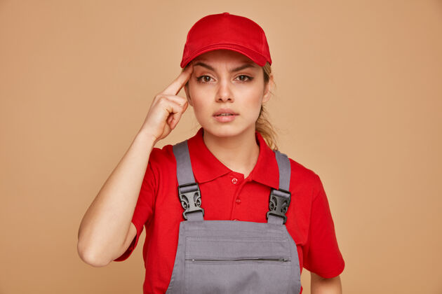 工人体贴的年轻女建筑工人穿着制服 戴着帽子做着思考的手势女性思想帽子
