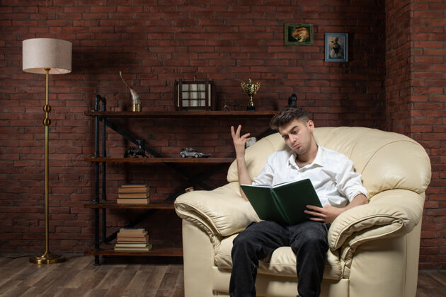 扶手椅年轻男性坐在沙发上看书的正面图在房间里工作晚上工作的房子里工作沙发年轻的男性