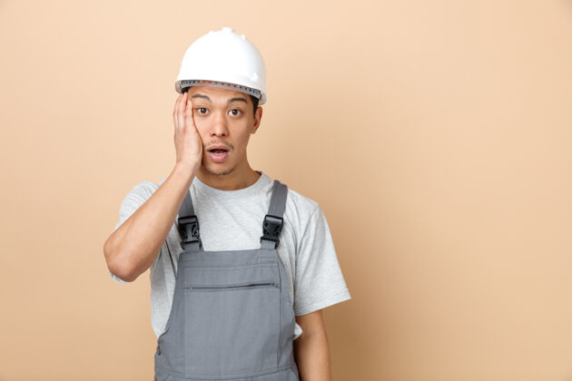 安全关心的年轻建筑工人戴安全帽和制服 手放在脸上手保持空间