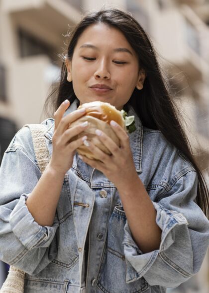 美味快乐的亚洲女人在户外吃汉堡垃圾食品小吃都市
