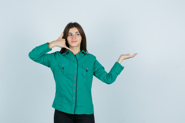 衬衫一个穿着绿色上衣 黑色裤子的年轻女孩 展示着打电话的姿势 把手掌放在一边 看上去很乐观 正对着前方女孩肖像成人