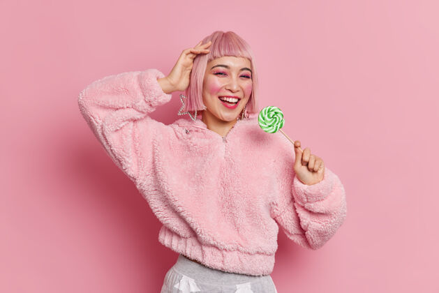 无忧无虑迷人时尚的亚洲年轻女子 粉色发型 手拿美味的绿色糖果 身着时尚外套可爱休闲棒棒糖