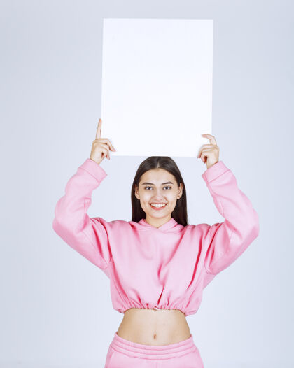女性穿着粉色睡衣的女孩头上举着一块空白的方形展示板 让每个人都能看到年轻人姿势服装