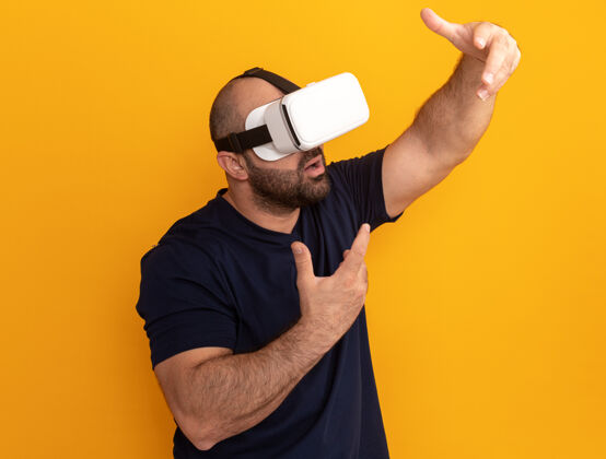 随意一个留着大胡子的男人穿着海军t恤 戴着一副虚拟现实的眼镜 站在橙色的墙上 双手在他面前做手势年轻