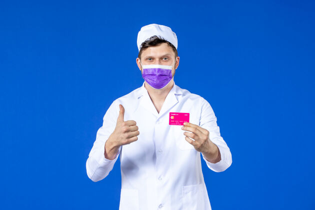男医生前视图中的男医生穿着医疗服和紫色面具持有信用卡在蓝色信用诉讼医学