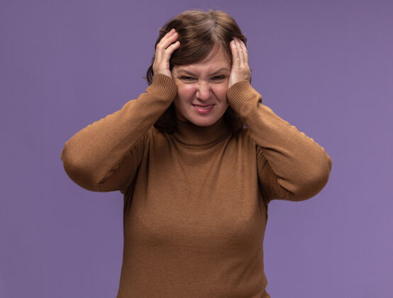 女人一个穿着棕色套头衫的中年妇女站在紫色的墙上 看上去很沮丧 很困惑站高领毛衣年龄