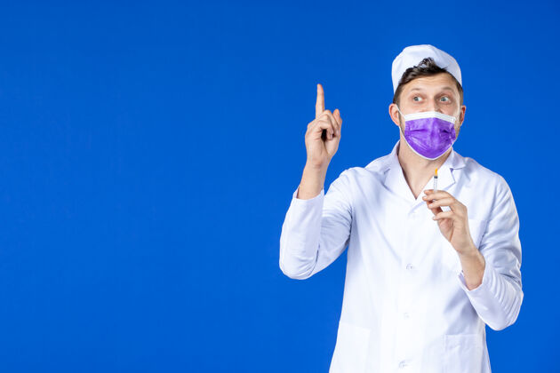 医院身穿医疗服 戴着紫色口罩的男医生正对着蓝色的脸拿着针剂西装治疗男医生