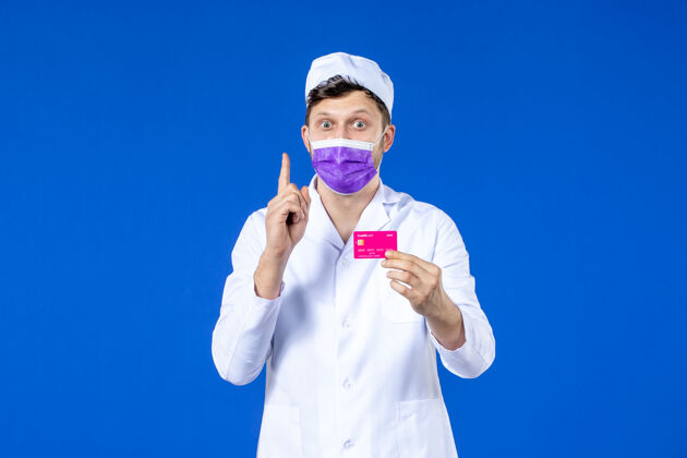 男医生前视图中的男医生穿着医疗服和面具持有信用卡的蓝色医院诉讼医学