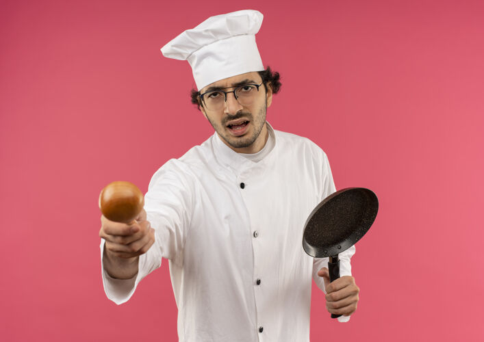 平底锅强调年轻的男厨师穿着厨师制服和眼镜拿着汤匙煎锅眼镜粉红男