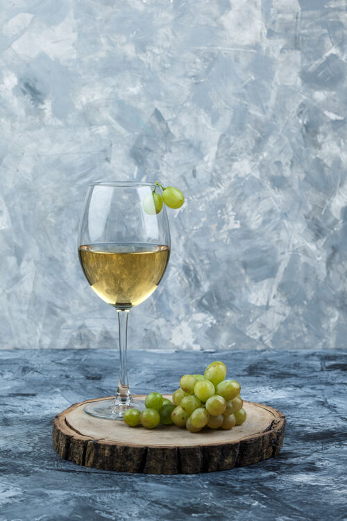 石膏一些绿色的葡萄和一杯葡萄酒在肮脏的石膏和木片背景上 侧视图多汁果汁健康