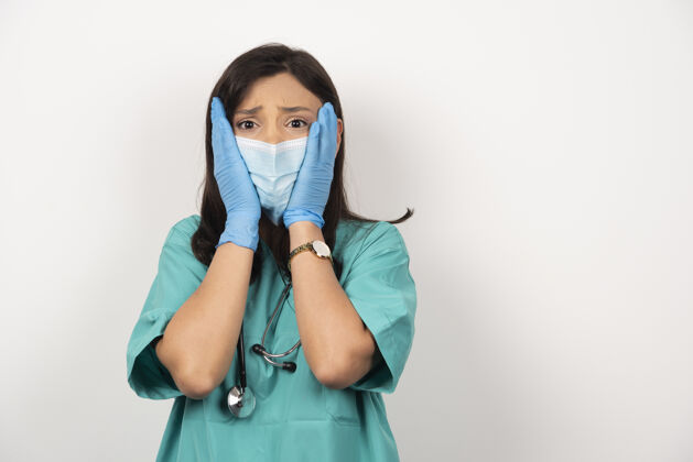 职业医生戴着医用面罩和手套 脸上挂着白色的背景 吓坏了她医疗女性医生