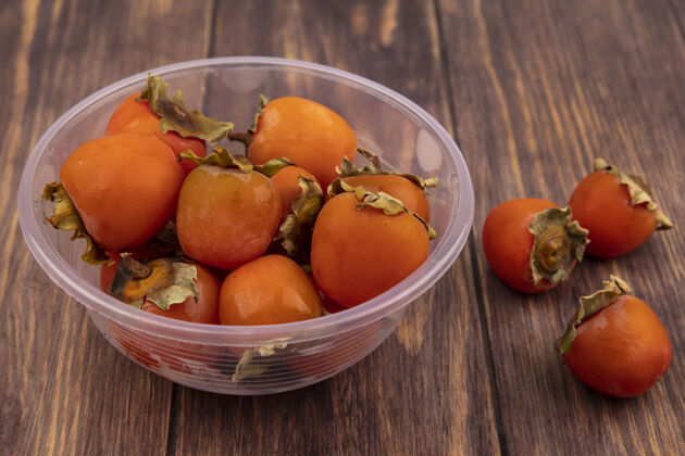 美味木制表面上透明塑料碗上柔软多汁的柿子俯视图新鲜午餐碗