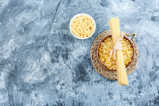 博洛尼亚灰色灰泥和柳条垫子背景上的碗里的各种意大利面顶视图晚餐美味盘子