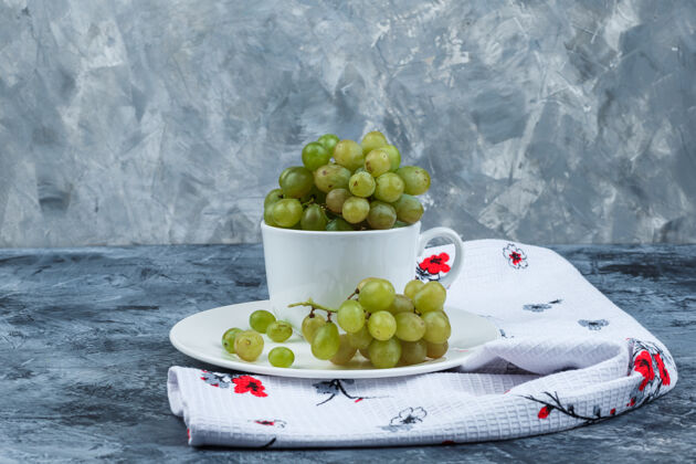 壁板侧视图绿色葡萄在白色的杯子和盘子上肮脏的石膏和厨房毛巾背景水平葡萄夏天果汁